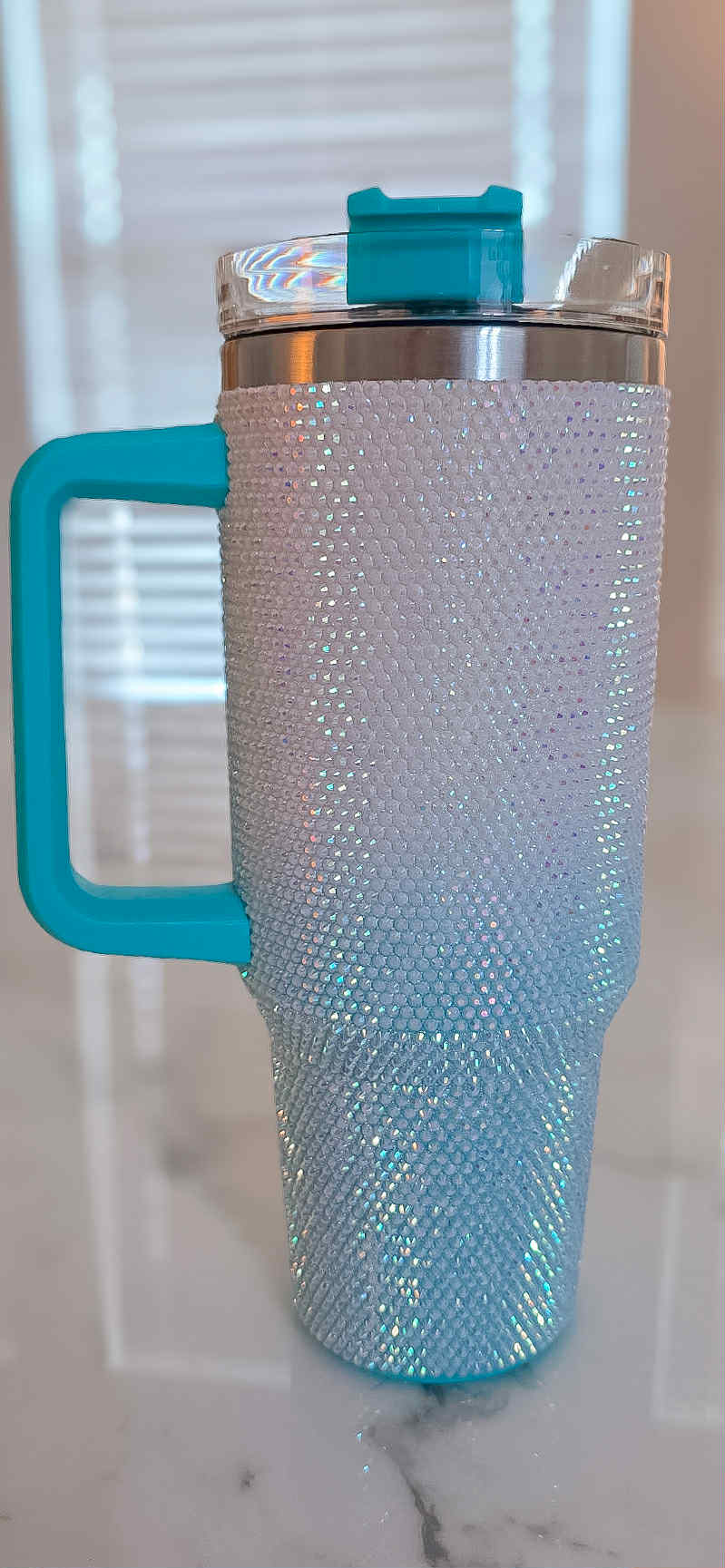 Travel mug with turquoise handle and lid on a marble surface